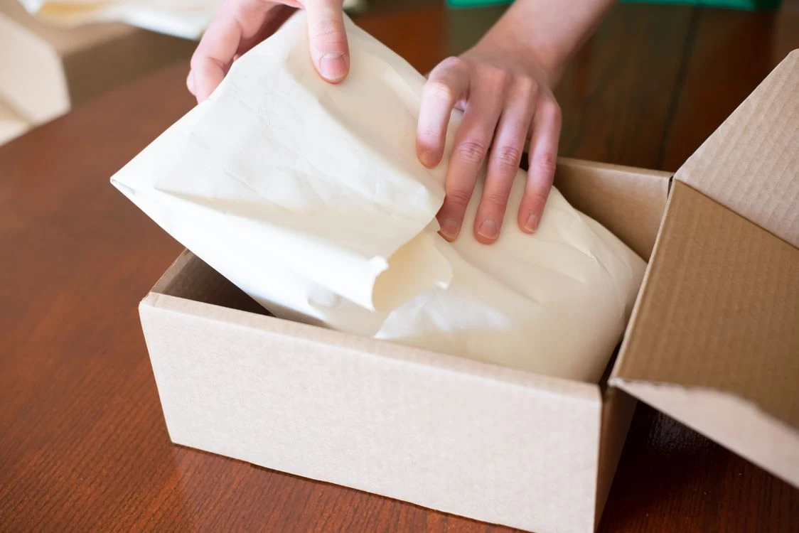 Kartonversand24 – Am Packtisch – Verpacken und Versand Hände verpacken eine Bestellung in einem Versandkarton